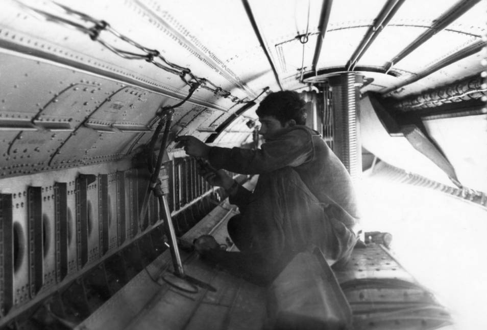 Механик выполняет работы в отсеке балочного держателя самолета Ту-95К, сидя на закрытой левой створке люка и опущенной балке БД-206. Вид по полету, правые створки отсека открыты, а левые закрыты