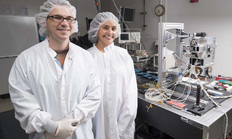 Члены команды Лаборатории холодного атома Дэвид Эвелин и Анита Сенгупта <br/> на фоне вакуумной камеры, в которой проводятся эксперименты <br/>по созданию ультра-холодного квантового газа